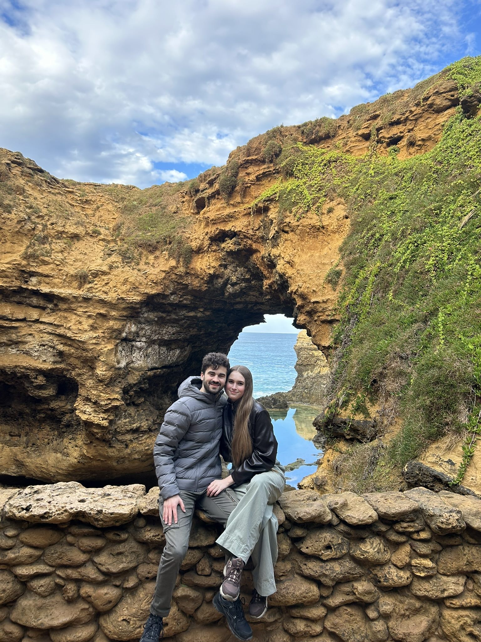 Callum and Celina sitting beneath a coastal rock arch